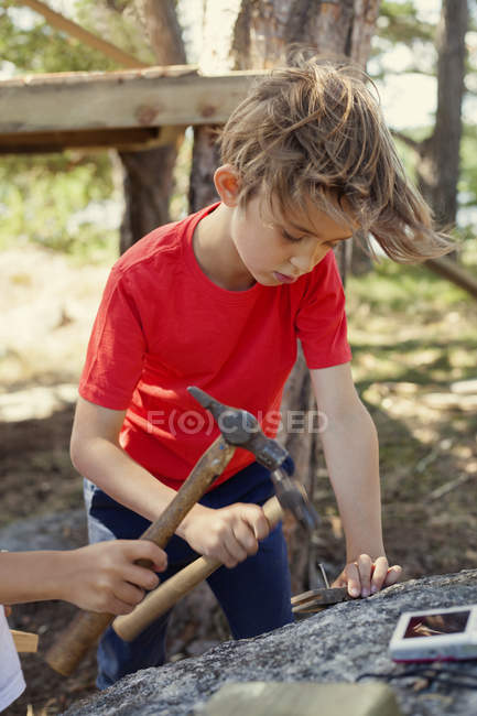Niño en camiseta roja golpeando con martillo - foto de stock