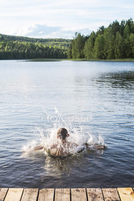 Vista trasera del niño saltando en el lago - foto de stock
