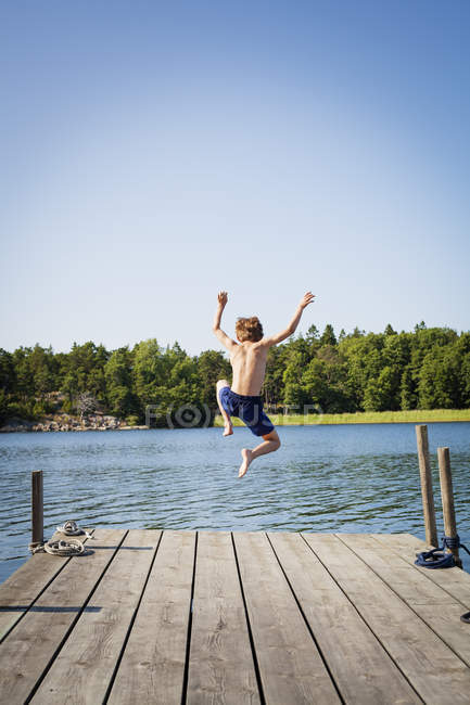 Visão traseira do menino mergulhando na água do molhe — Fotografia de Stock
