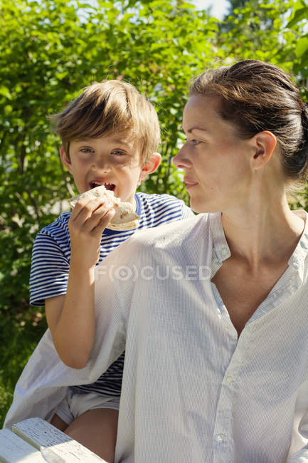 Madre sentada cerca de hijo comiendo sándwich, enfoque selectivo - foto de stock