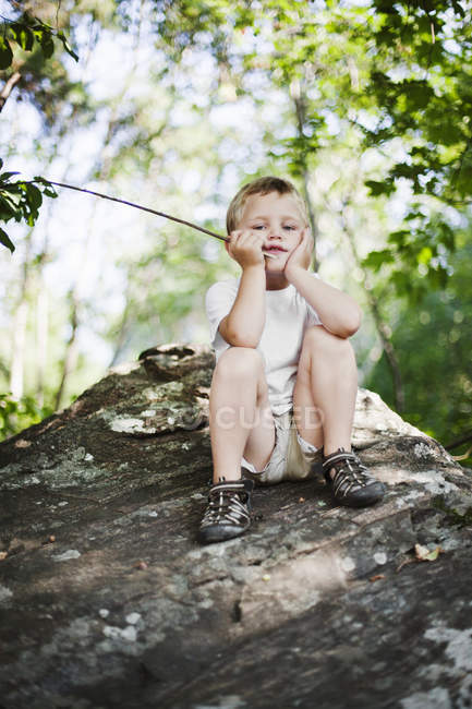 Портрет мальчика, сидящего на скале, фокус на переднем плане — стоковое фото