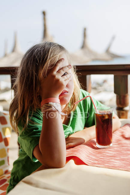 Дівчина сидить за столом і прикриває обличчя рукою — стокове фото