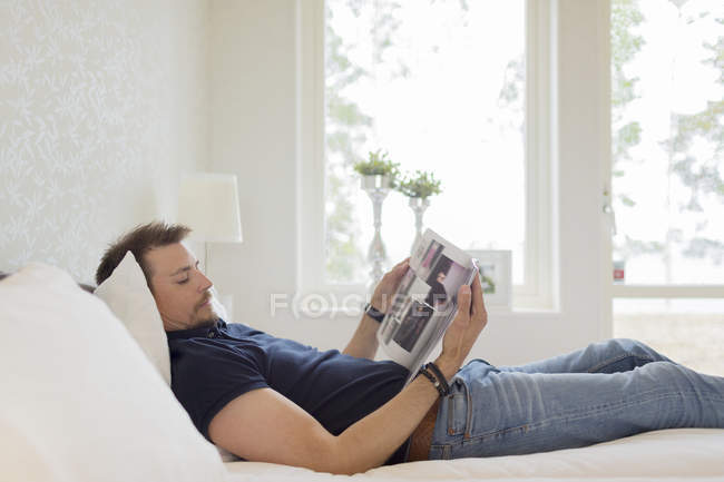 Человек читает журнал в постели, дифференциальный фокус — стоковое фото