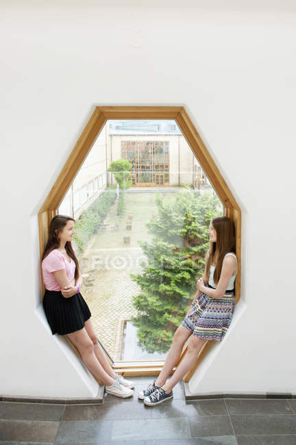 Chicas apoyadas en el marco de la ventana y hablando - foto de stock