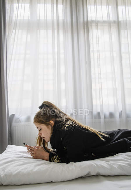 Боковой вид женщины, использующей смартфон на кровати — стоковое фото