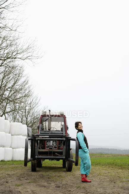 Фермер в резиновых сапогах прислонился к трактору — стоковое фото