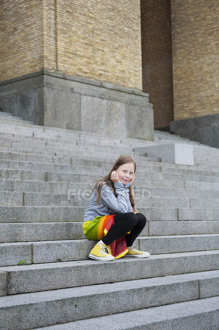 Retrato de la chica sentada en los escalones y mirando a la cámara - foto de stock