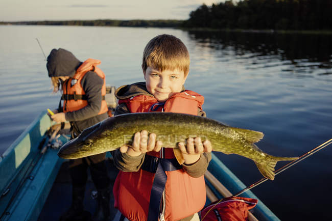 Niño en barco mostrando pescado capturado con chica en el fondo - foto de stock