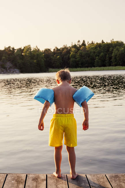 Visão traseira do menino vestindo asas de água em pé no molhe — Fotografia de Stock