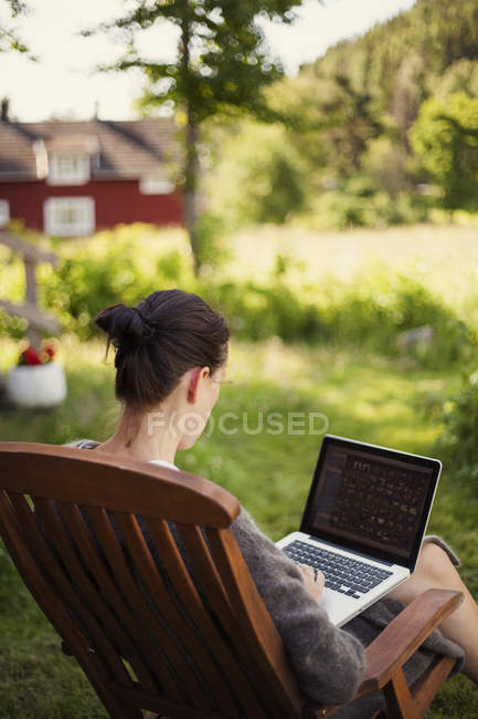 Mulher usando laptop no jardim, foco em primeiro plano — Fotografia de Stock