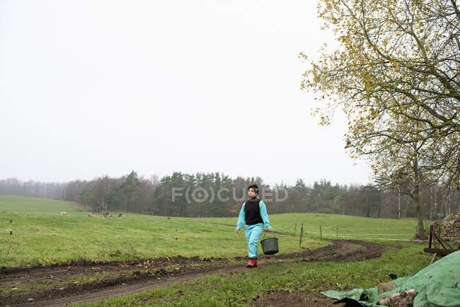Agricultor en botas de goma llevando cubo - foto de stock