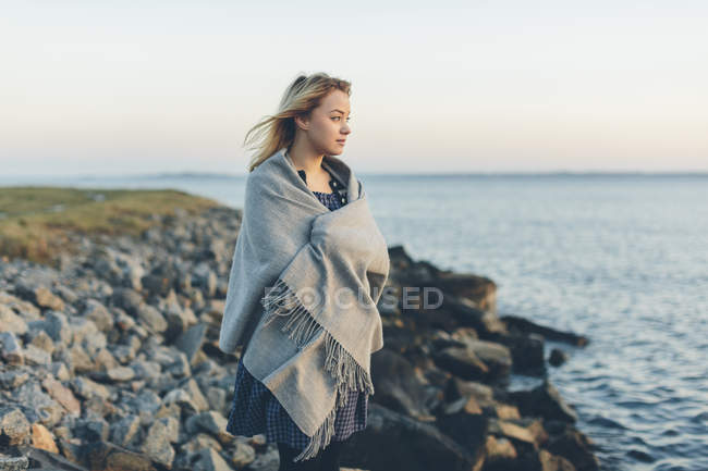 Mujer joven envuelta en chal mirando al mar - foto de stock