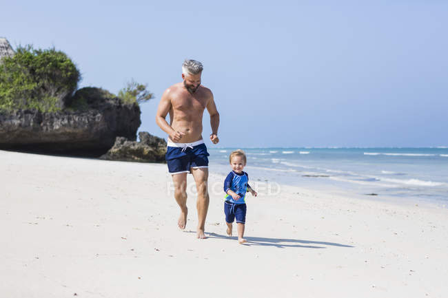 Отец и сын бегут по пляжу Диани, Кения — стоковое фото