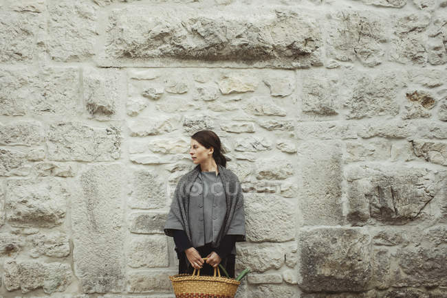 Giovane donna in piedi da parete di pietra che tiene cesto — Foto stock