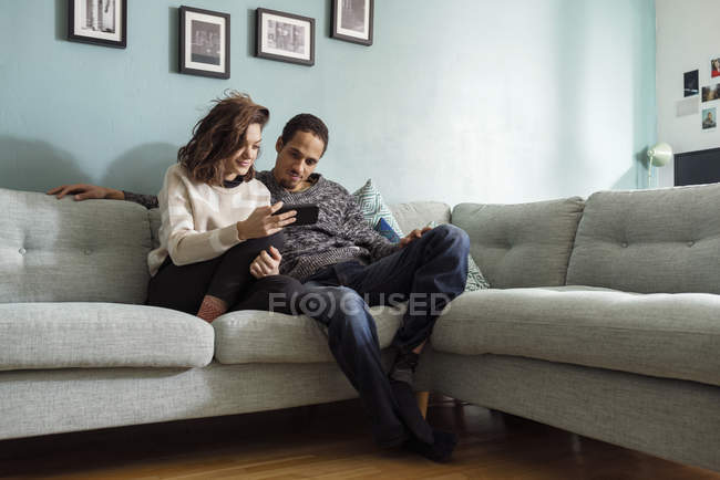 Молодая пара сидит на диване и смотрит на смартфон — стоковое фото
