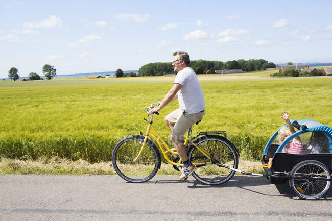 Vista lateral do pai de ciclismo com a filha em reboque de bicicleta — Fotografia de Stock
