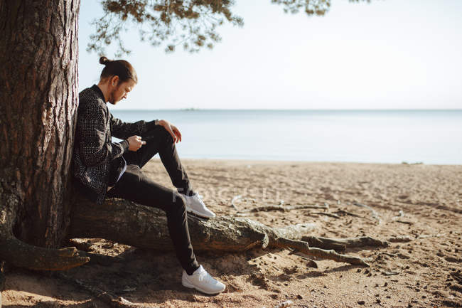 Junger Mann benutzt Smartphone am Strand — Stockfoto