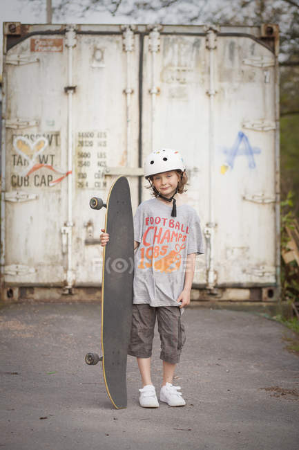Portrait of boy with skateboard in front of gate — Stock Photo