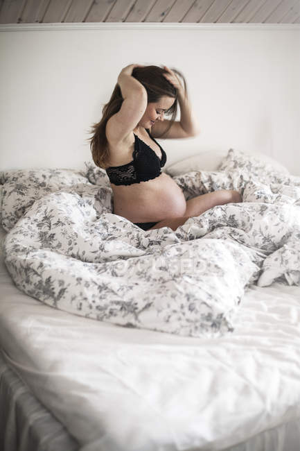 Jeune femme enceinte assise sur le lit — Photo de stock