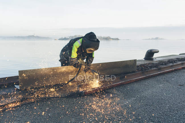 Homem de soldagem ao lado do mar, foco em primeiro plano — Fotografia de Stock