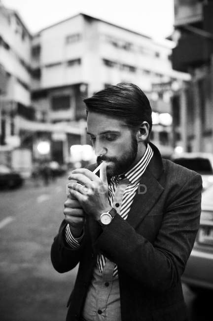Человек, стоящий на улице и закуривающий сигарету — стоковое фото