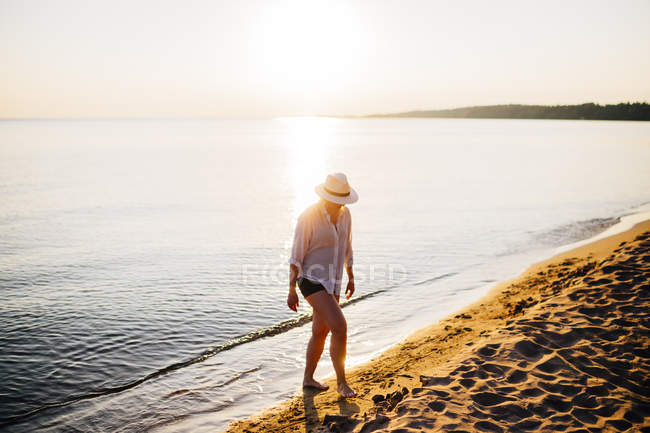 Вид сбоку на женщину, идущую по пляжу летом — стоковое фото