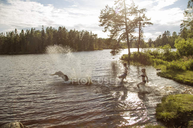 Молодой человек с детьми играет на озере на закате — стоковое фото