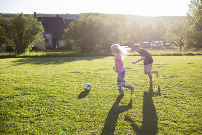 Side view of girl and boy playing soccer in garden — Stock Photo