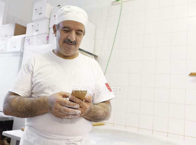 Зрелый шеф-повар с помощью смартфона на коммерческой кухне — стоковое фото