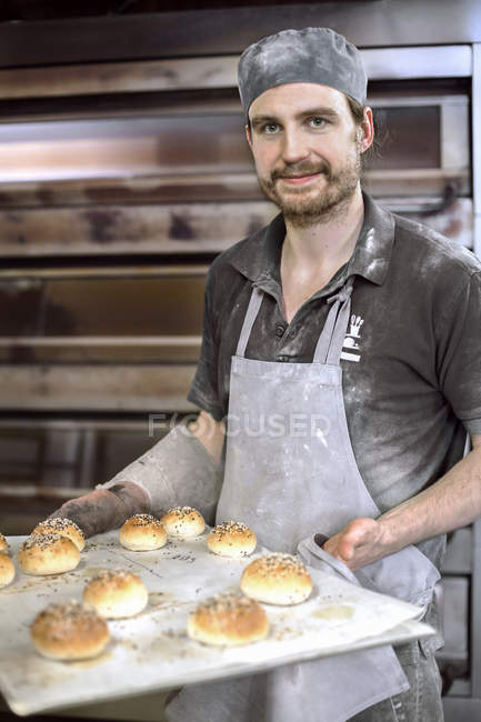 Пекарь держит лист со свежими булочками, дифференциальный фокус — стоковое фото