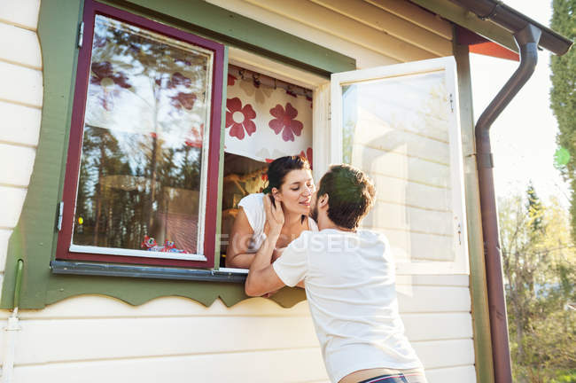 Casal beijando embora janela de casa — Fotografia de Stock