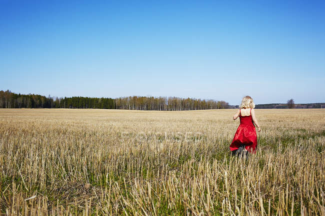 Chica usando vestido rojo caminando en el campo - foto de stock