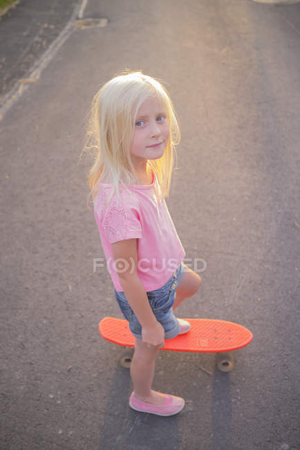 Portrait of girl riding red shortboard in street, differential focus — Stock Photo