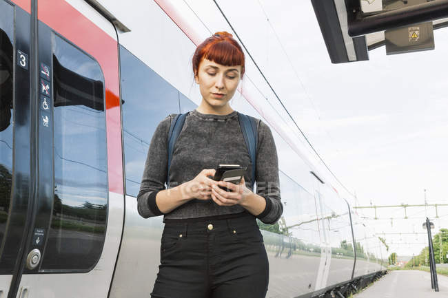Женщина смотрит на смартфон на железнодорожной платформе — стоковое фото