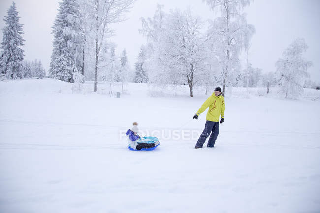 Vista lateral del padre tirando de la niña en el trineo en invierno - foto de stock