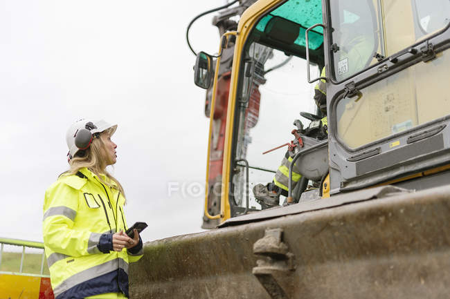 Woman talking to man inside earth mover at construction site, differential focus — Stock Photo