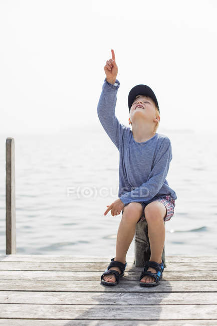 Boy sitting on pole on wooden jetty — Stock Photo