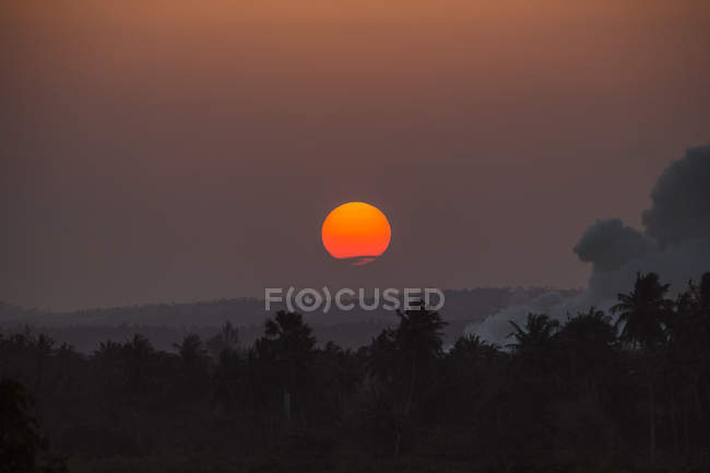 Vista panorámica de la puesta de sol sobre los árboles con humo en Kenia - foto de stock