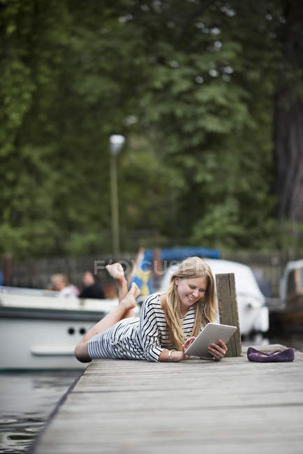 Porträt einer Frau, die mit digitalem Tablet auf einem Holzsteg liegt — Stockfoto