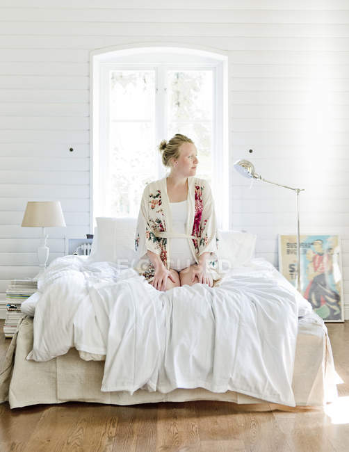 Schwangere Frau im mittleren Erwachsenenalter sitzt auf Bett und schaut weg — Stockfoto