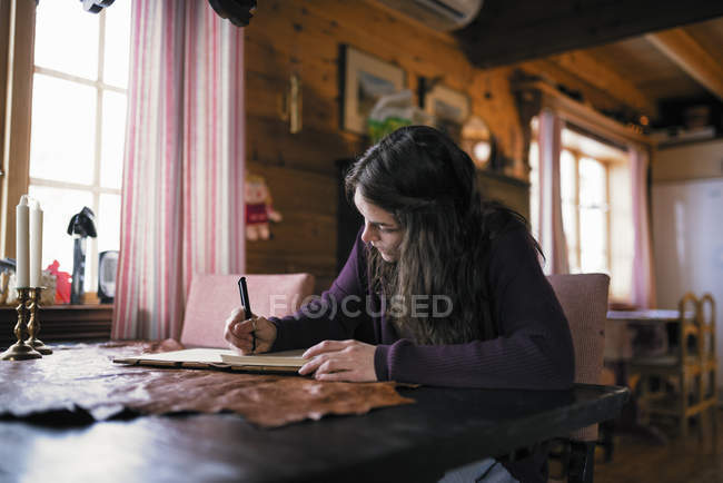 Jeune femme assise à table et écrivant dans la laiterie — Photo de stock