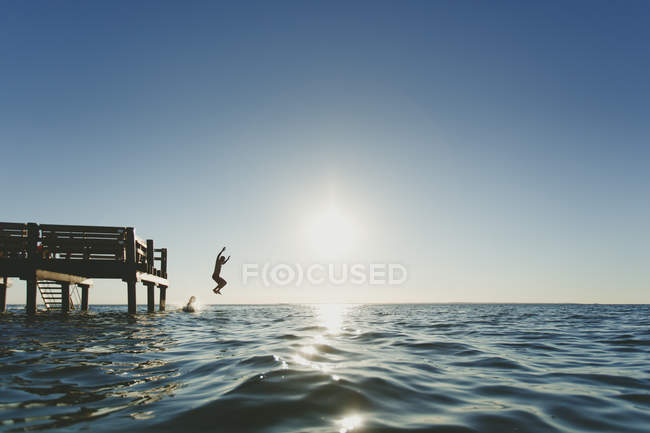 Вид сбоку на двух людей, прыгающих в море — стоковое фото