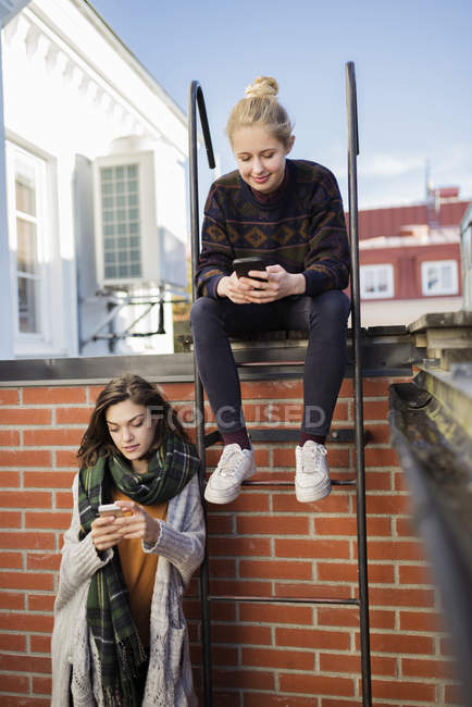 Две молодые женщины используют смартфоны на крыше — стоковое фото