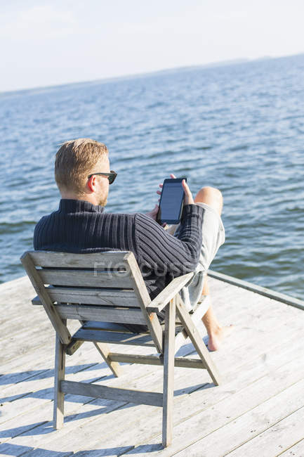 Man using digital tablet on jetty, focus on foreground — Stock Photo
