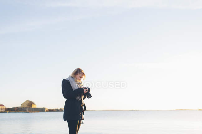 Femme tenant caméra par la mer, se concentrer sur l'avant-plan — Photo de stock