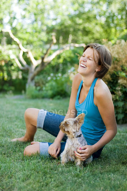 Mujer sentada en la hierba con terrier y riendo - foto de stock