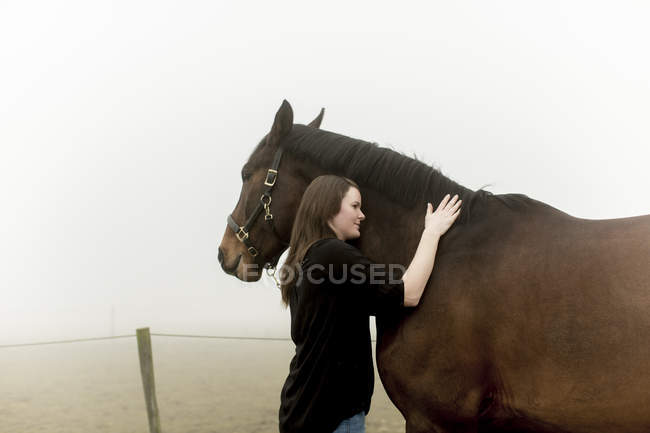 Femme mi-adulte avec cheval sur un chemin de terre dans le brouillard — Photo de stock