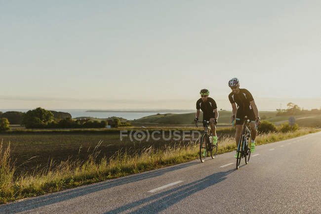 Two men cycling under clear sky, focus on foreground — Stock Photo