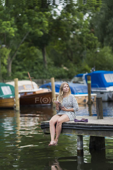Портрет женщины, сидящей на деревянном пирсе с помощью цифрового планшета — стоковое фото