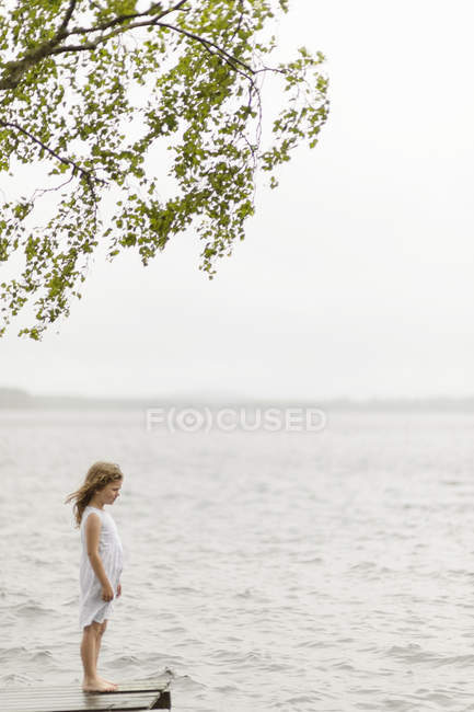 Vista lateral da menina de pé no molhe pelo lago — Fotografia de Stock